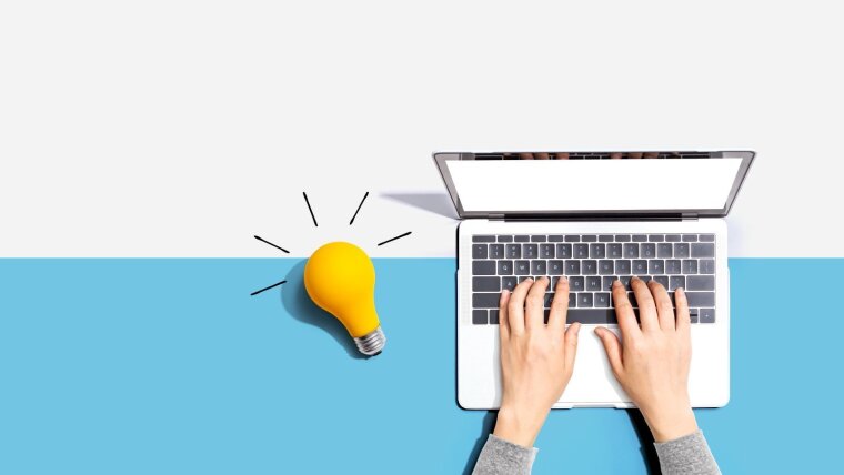Hände tippen am Laptop und daneben leuchtet eine Glühbirne