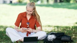 Junge Person sitzt auf Wiese und schaut auf das Smartphone