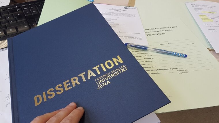 Symbolbild PhD office: A dissertation and the doctoral degree regulations are on a desk.