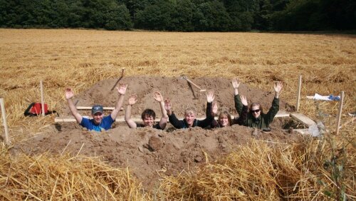 Studierende stehen in einem auf einem Feld gegrabenen Loch.